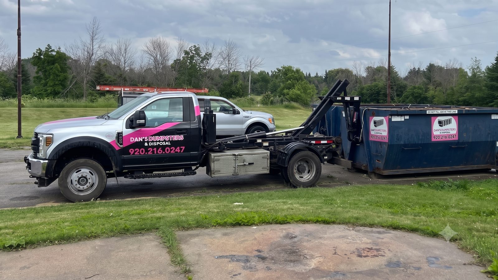 Dan's Dumpsters & Disposal hook-lift truck marked 920.216.0247 loading a dumpster in the Fox Valley, Wisconsin