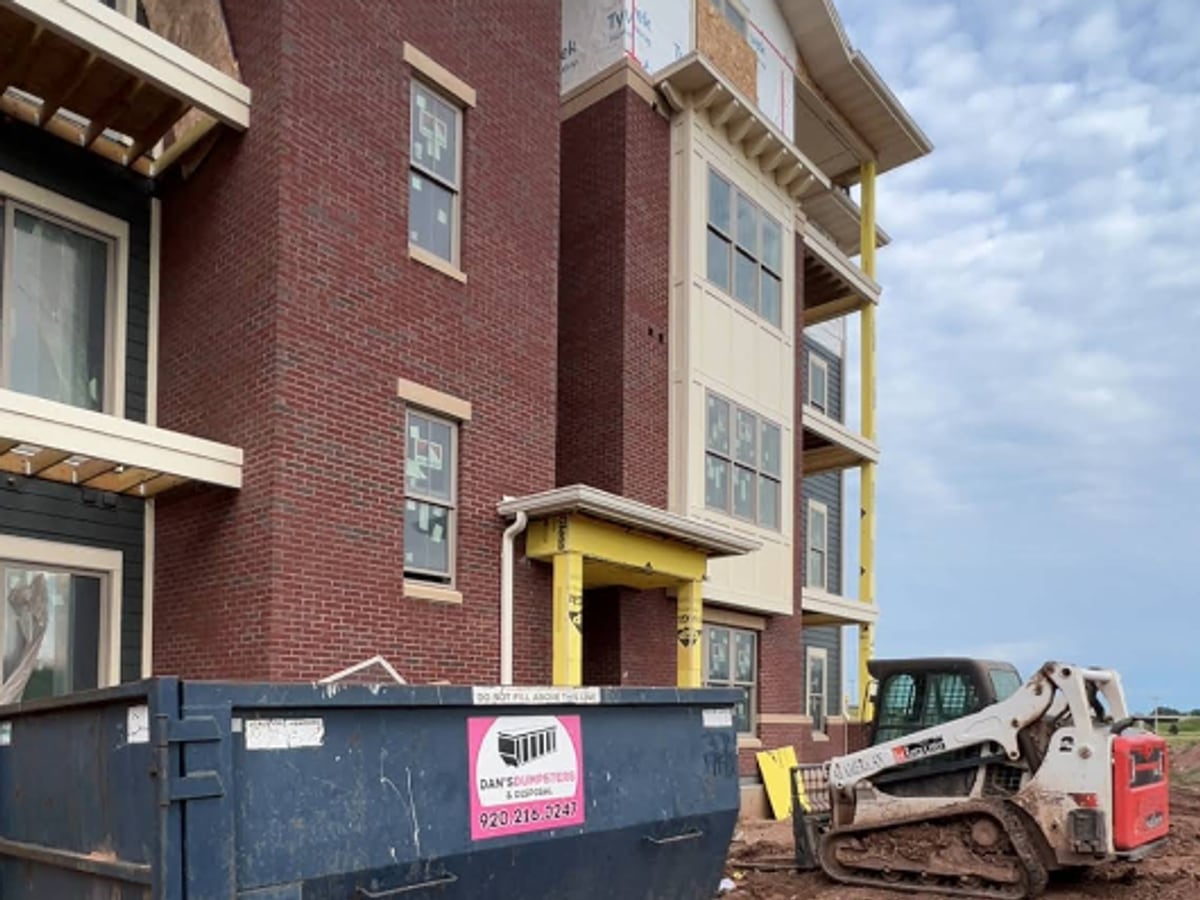 A roll-off dumpster and skid steer at a brick apartment building during a property cleanout