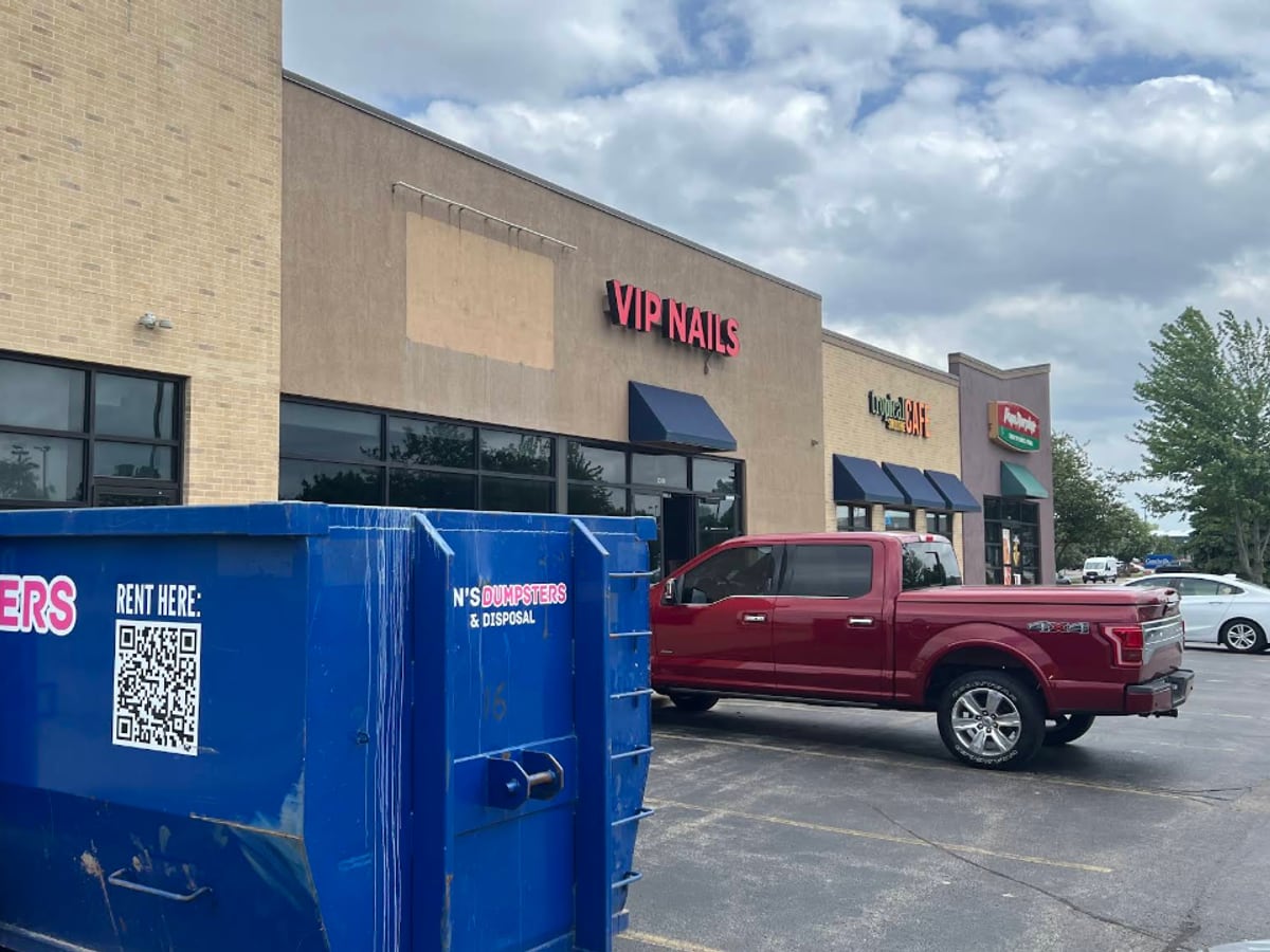 A Dan's Dumpsters roll-off dumpster parked outside a strip-mall business for a commercial cleanout