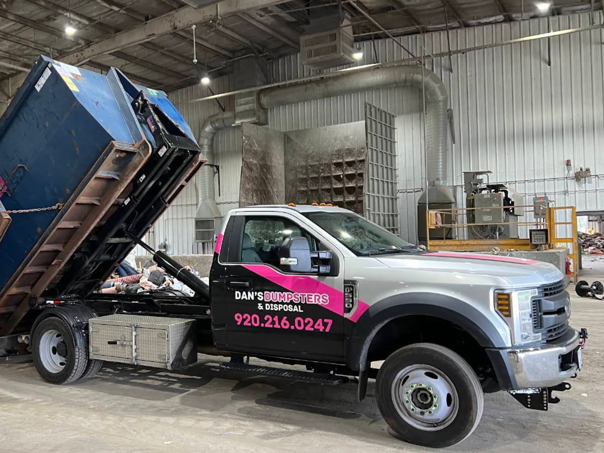 A Dan's Dumpsters truck emptying a loaded roll-off dumpster at a disposal facility