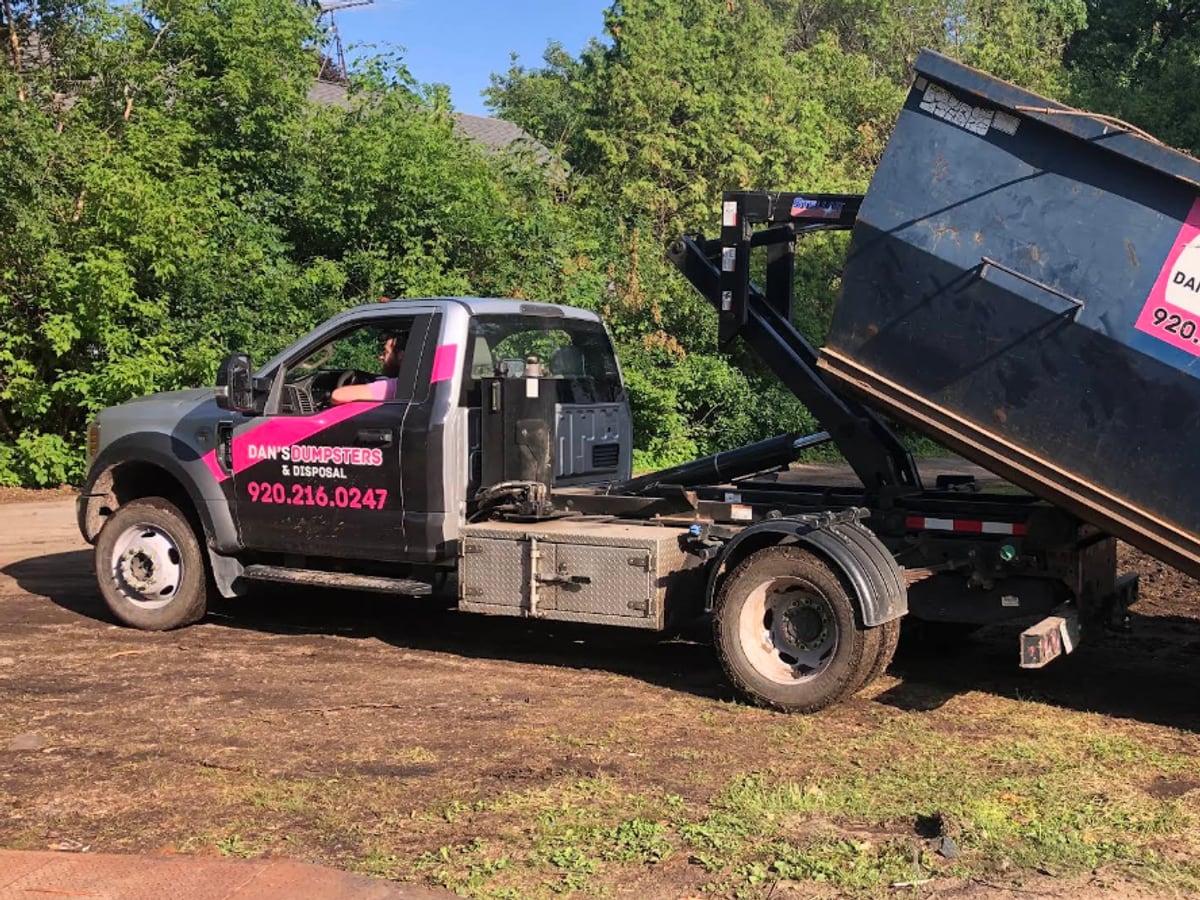 A Dan's Dumpsters truck tilting a roll-off dumpster off its bed to set it down at a job site