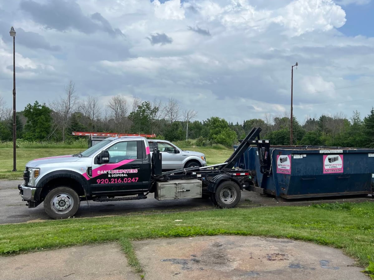A silver Dan's Dumpsters truck with a roll-off dumpster on an open lot in the Fox Valley