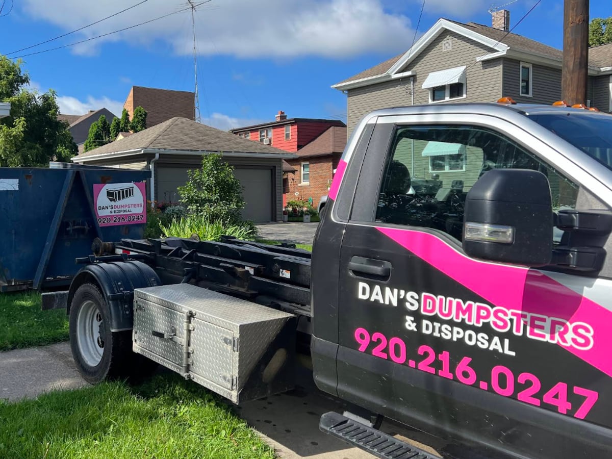 The grey Dan's Dumpsters & Disposal hooklift truck with pink wrap and phone number, carrying a roll-off